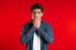 © kohanova1991 - Young man sneezes into tissue. Isolated guy is sick, has a cold or allergic reaction. Coronavirus, epidemic 2020, illness concept. Red background