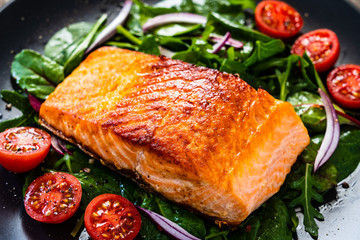 Fried salmon steak with vegetables on wooden table