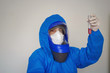 A man in a blue protective suit holds a test tube in his hands. The concept of open vaccines against coronavirus