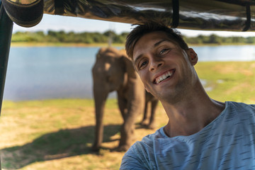 young man taking a selfie from a safari jeep with an asian elephant in the background