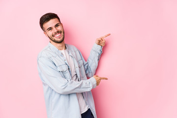 Young caucasian business man posing in a white background isolated excited pointing with forefingers away.< mixto >