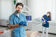 © Тарас Нагирняк - Young handsome and bearded dentist holding folder, while his assistant preparing equipment.