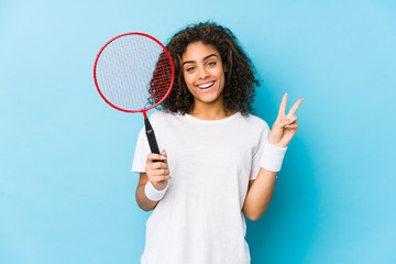 Young african american woman playing badminton joyful and carefree showing a peace symbol with fingers.