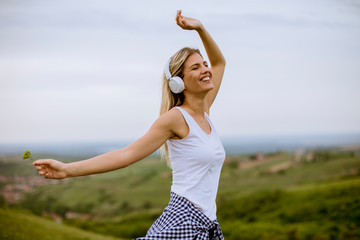 Wall Mural - Happy young woman in nature listening to music on headphones