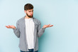 © Asier - Young caucasian man isolated on blue background doubting and shrugging shoulders in questioning gesture.