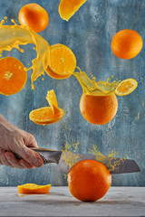 Sticker - Freshly cut orange levitation. A knife cuts an orange. Oranges sprinkle with juice and juice flows from different directions. Flying slices of oranges, on a blue background