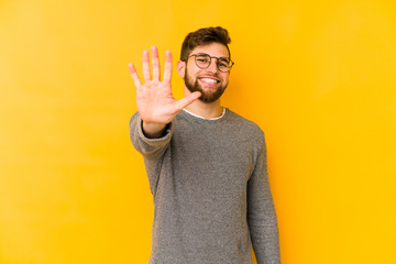 Wall Mural - Young caucasian man isolated on yellow background smiling cheerful showing number five with fingers.