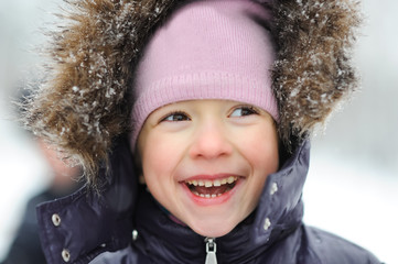 Little girl close-up portrait smiling and walking in the winter outdoors. Children outdoor. Happy kid, child having fun in beautiful winter park during snowfall.