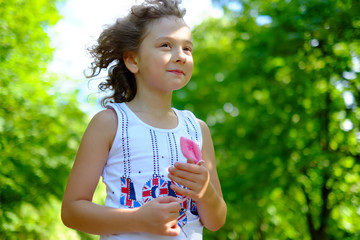 Wall Mural - Cute little girl outdoors with curly hair in the wind. Smiling, happy toddler child, kid on a windy day breathing fresh air in the green park on the nature at summer or spring.