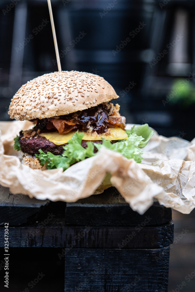 Obraz na płótnie Burger owinięty w papier ekologiczny w tle industrialny styl, czarne tło. Hamburger z mięsem ze świeżymi dodatkami w bułce sezamowej.  w salonie