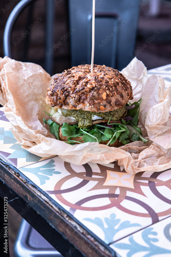 Obraz na płótnie Świeżo grillowany burger leży na stoliku azelejos. Kanapka w amerykańskim stylu zawinięta w papier ekologiczn, street food. Restauracja w industrialnym stylu.  w salonie