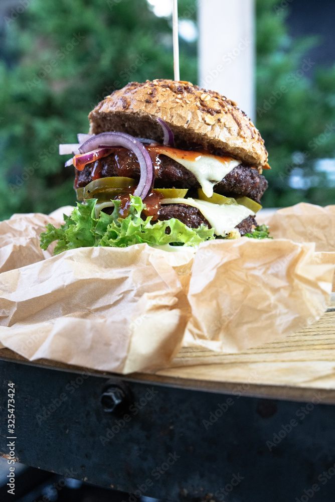 Obraz na płótnie Burger na industrialnym stole w ekologicznym papierze. Duży lunch, burger meksykański grillowany na ogrodzie. Burger w bułce pełnoziarnistej. w salonie