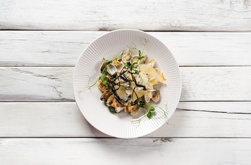 Spinach pasta with vongole in a creamy sauce on white wood background. Top view..