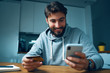 © baranq - Young man sitting at home late and ordering online with smartphone and credit card