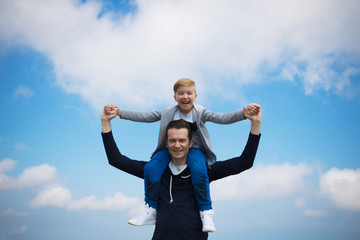 Cheerful boy and his father having fun against the sky.