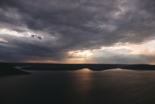 Beautiful View Of Sun Rays From Dark Clouds Above Lake. Sunset Light Over Hill And River Landscape. Dramatic Moody Scenery. Bakota Lake And Dniester River In Ukraine