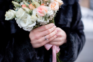 beautiful girl bride in a black coat holds in her hands a wedding bouquet of flowers