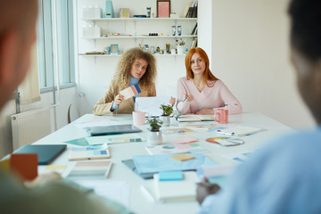 Wall Mural - Portrait of two female designers sitting opposite two men while discussing creative project, copy space