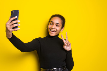 Wall Mural - Portrait of a happy young woman take selfie standing isolated on yellow background