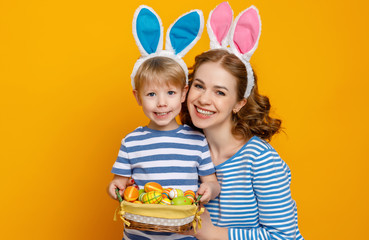 Wall Mural - Happy easter! family mother and child son with ears hare getting ready for holiday on colored yellow background.