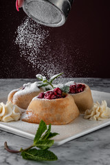 female hand sprinkling icing sugar on white plate with pancakes, mint, butter and red cherry on a white marble table served in restaurant, concept of russian festival meal maslenitsa or shrovetide