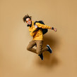 © FAB.1 - Young teen boy in comfortable clothing, sneakers, sunglasses and backpack jumping and feeling cool over yellow wall background