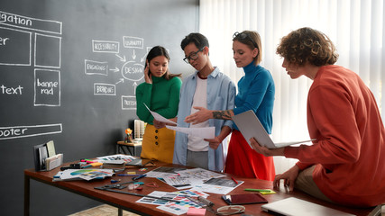 Wall Mural - website usability. group of four young designers discussing new project and sharing ideas while havi