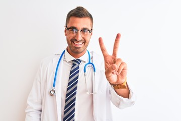 Canvas Print - Young handsome doctor man wearing stethoscope over isolated background smiling looking to the camera showing fingers doing victory sign. Number two.