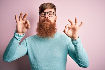 Sticker - Handsome Irish redhead man with beard wearing glasses over pink isolated background relaxed and smiling with eyes closed doing meditation gesture with fingers. Yoga concept.