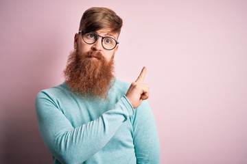 Poster - Handsome Irish redhead man with beard wearing glasses over pink isolated background Pointing with hand finger to the side showing advertisement, serious and calm face