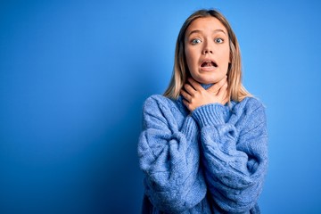 Young beautiful blonde woman wearing winter wool sweater over blue isolated background shouting and suffocate because painful strangle. Health problem. Asphyxiate and suicide concept.