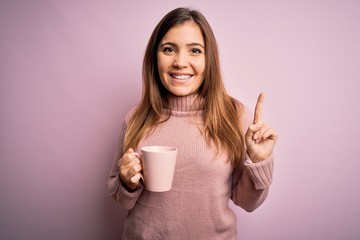 Sticker - Young blonde woman drinking a cup of coffee over pink isolated background surprised with an idea or question pointing finger with happy face, number one