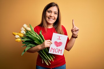 Sticker - Beautiful woman holding paper with love mom message and tulips celebrating mothers day surprised with an idea or question pointing finger with happy face, number one