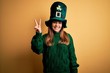 © Krakenimages.com - Young beautiful brunette woman wearing green hat on st patricks day celebration showing and pointing up with fingers number two while smiling confident and happy.