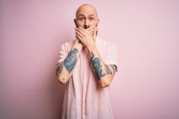 Poster - Handsome bald man with beard and tattoo wearing casual shirt over isolated pink background shocked covering mouth with hands for mistake. Secret concept.