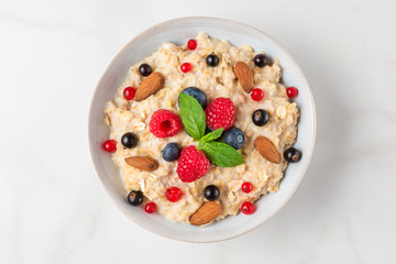 Wall Mural - Bowl of oatmeal porridge with fresh berries, almonds and mint with for healthy diet breakfast on white table