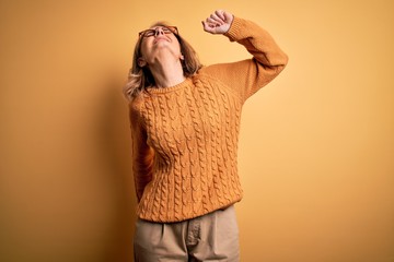 Wall Mural - Middle age beautiful blonde woman wearing casual sweater and glasses over yellow background stretching back, tired and relaxed, sleepy and yawning for early morning