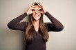 © Krakenimages.com - Young beautiful girl wearing casual sweater standing over isolated white background doing ok gesture like binoculars sticking tongue out, eyes looking through fingers. Crazy expression.