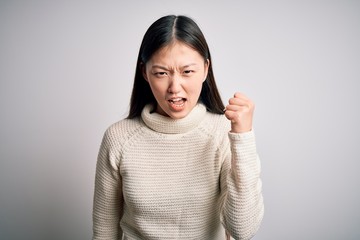 Poster - Young beautiful asian woman wearing casual sweater standing over isolated background angry and mad raising fist frustrated and furious while shouting with anger. Rage and aggressive concept.