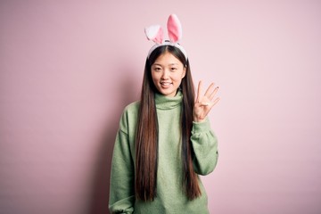 Canvas Print - Young asian woman wearing cute easter bunny ears over pink background showing and pointing up with fingers number four while smiling confident and happy.