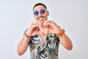 Poster - Young handsome man wearing Hawaiian sumer shirt and blue sunglasses over isolated background smiling in love showing heart symbol and shape with hands. Romantic concept.