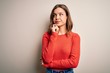 © Krakenimages.com - Young blonde girl wearing casual red sweater over isolated background with hand on chin thinking about question, pensive expression. Smiling with thoughtful face. Doubt concept.