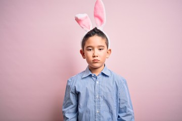 Sticker - Young little boy kid wearing easter bunny ears over isolated pink background with serious expression on face. Simple and natural looking at the camera.