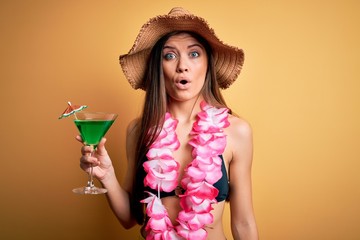 Beautiful woman with blue eyes on vacation wearing bikini and hawaiian lei drinking cocktail scared in shock with a surprise face, afraid and excited with fear expression