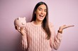 © Krakenimages.com - Young beautiful brunette woman holding piggy bank saving money for retirement very happy and excited, winner expression celebrating victory screaming with big smile and raised hands