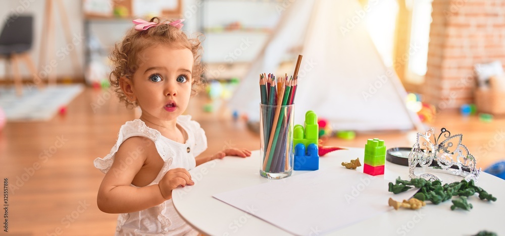 Beautiful caucasian infant playing with toys at colorful playroom. Happy and playful drawing with color pencils at kindergarten. - obrazy, fototapety, plakaty 
