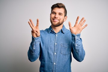 Young handsome blond man with beard and blue eyes wearing casual denim shirt showing and pointing up with fingers number eight while smiling confident and happy.