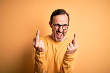 Poster - Middle age hoary man wearing casual sweater and glasses over isolated yellow background Showing middle finger doing fuck you bad expression, provocation and rude attitude. Screaming excited