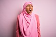 © Krakenimages.com - Young African American afro woman wearing muslim hijab over isolated pink background angry and mad screaming frustrated and furious, shouting with anger. Rage and aggressive concept.