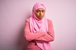 © Krakenimages.com - Young African American afro woman wearing muslim hijab over isolated pink background skeptic and nervous, disapproving expression on face with crossed arms. Negative person.